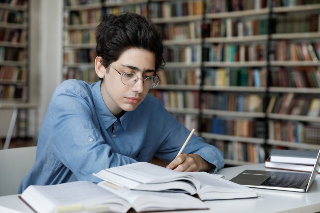 High school student writing in a library, representing college essay coaching support