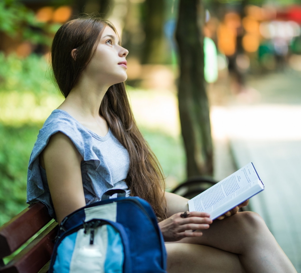 High school student sitting outdoors with a notebook, reflecting as homework from a college essay coaching session